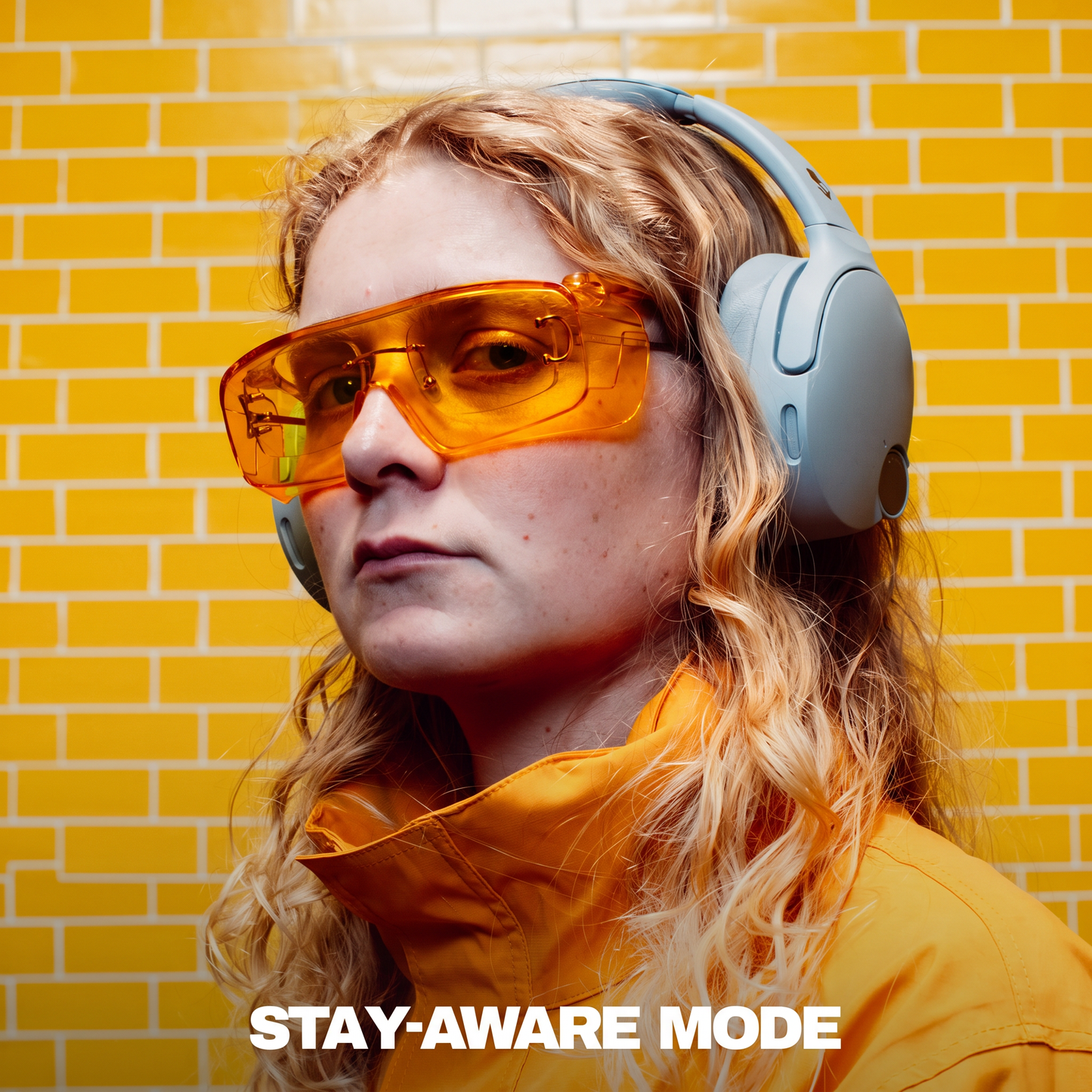 Person wearing orange sunglasses and a yellow jacket with a yellow brick wall background | Cement