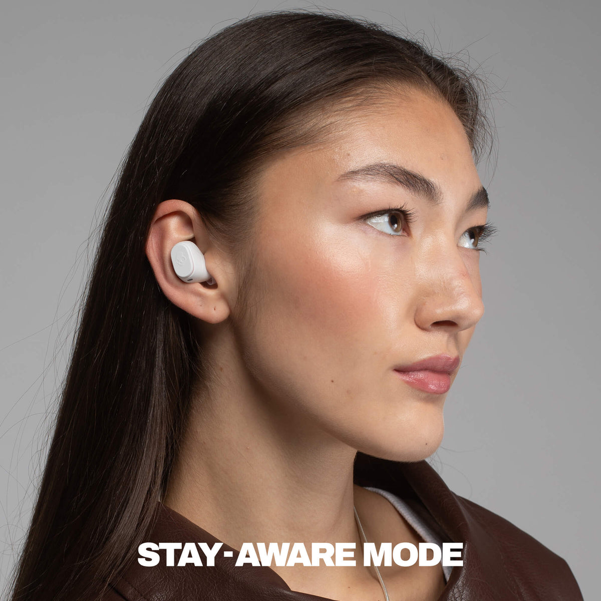 Person wearing wireless earbuds with 'Stay-Aware Mode' text on a gray background | Bone