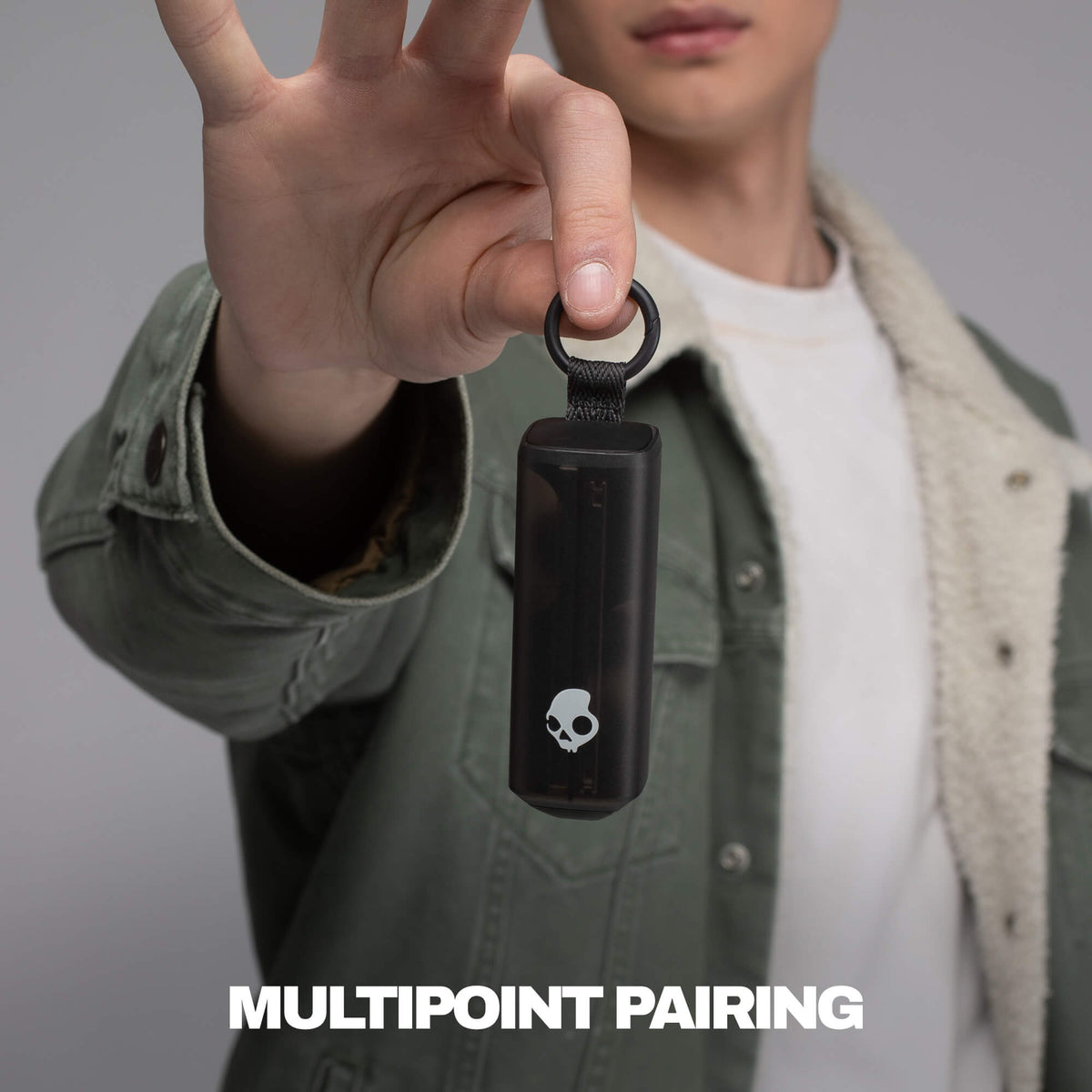 Person holding a black device with a skull logo, labeled 'Multipoint Pairing', against a gray background. | True Black