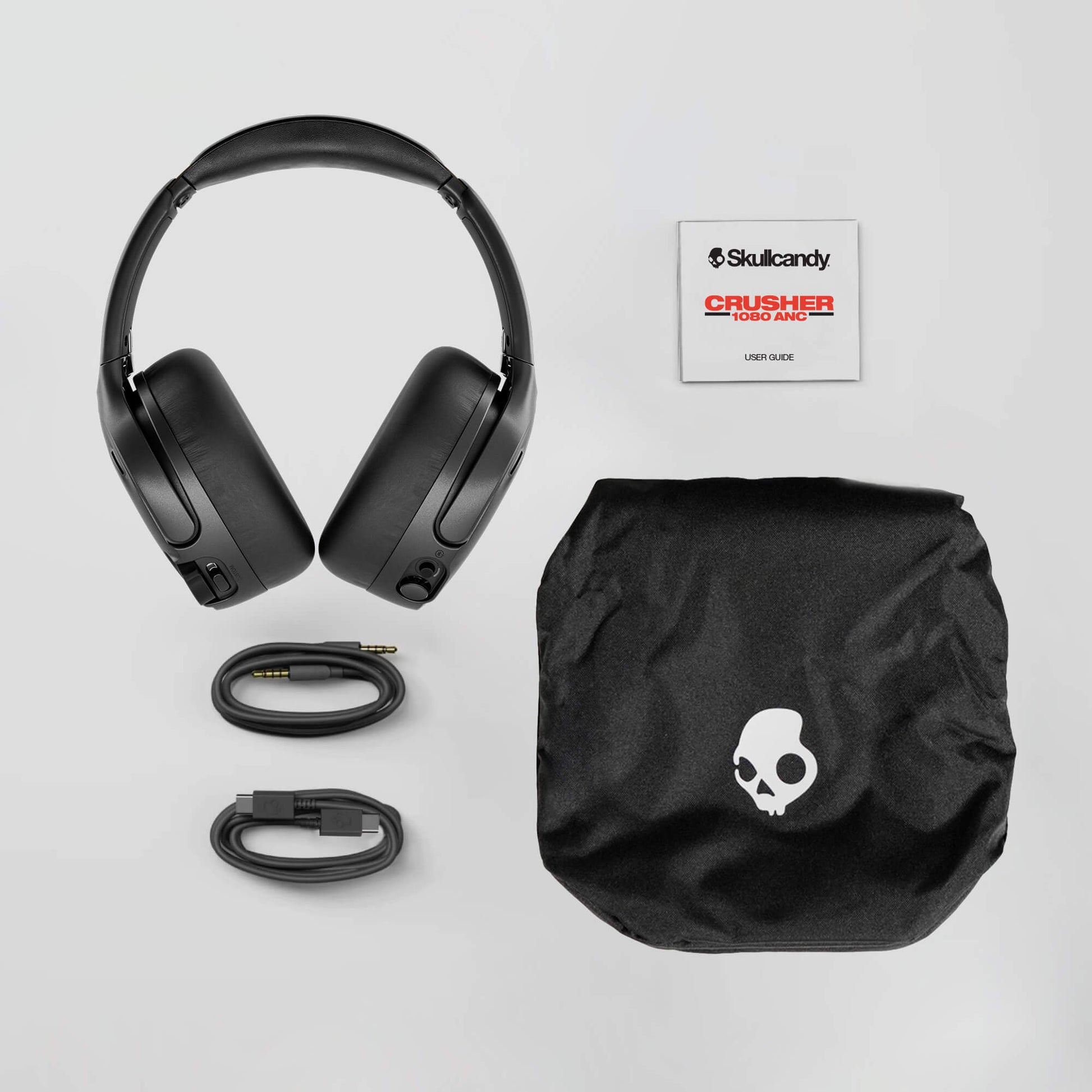 Black headphones with accessories and Skullcandy logo on a light gray background | Candy