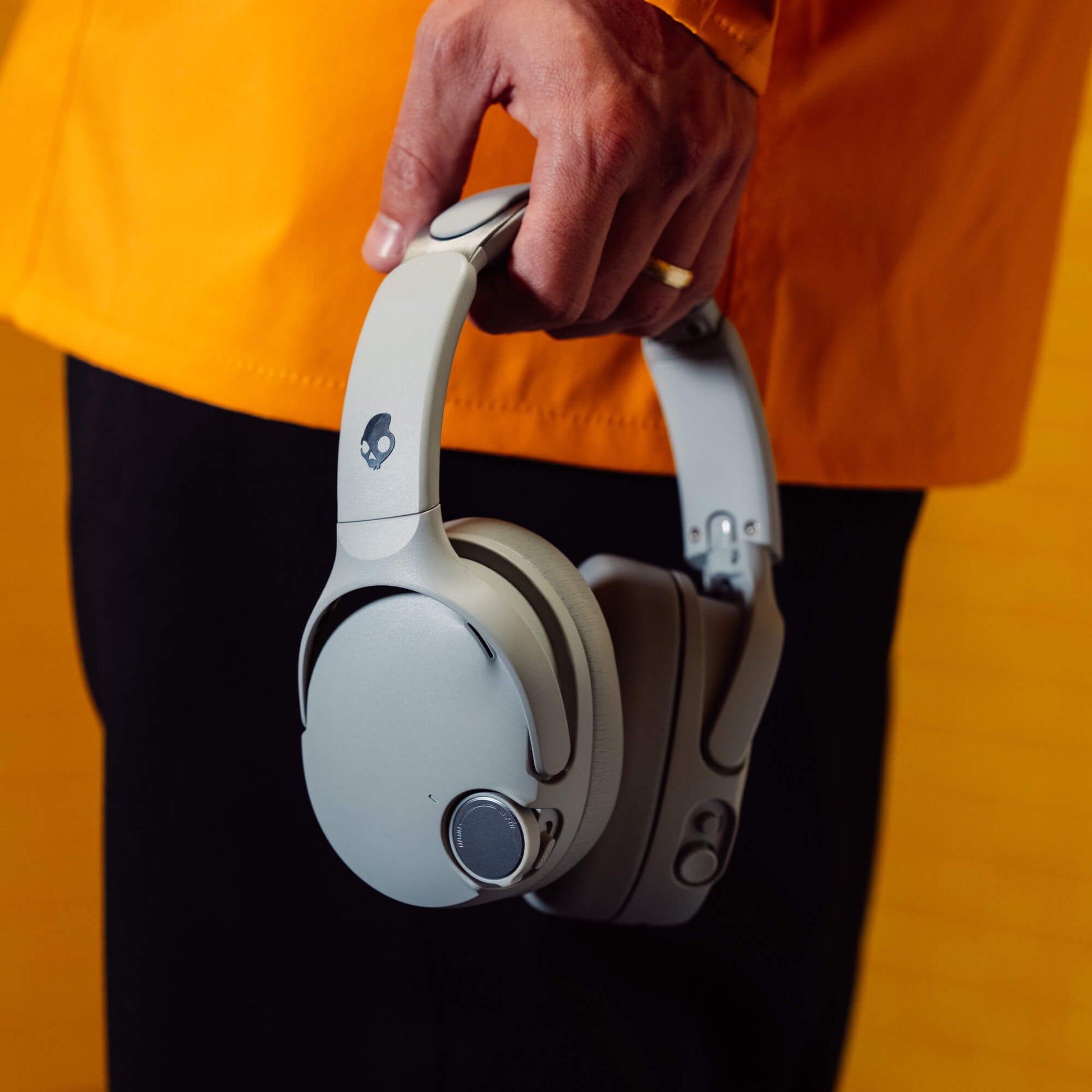 White headphones held by a person wearing an orange jacket and black pants. | Cement