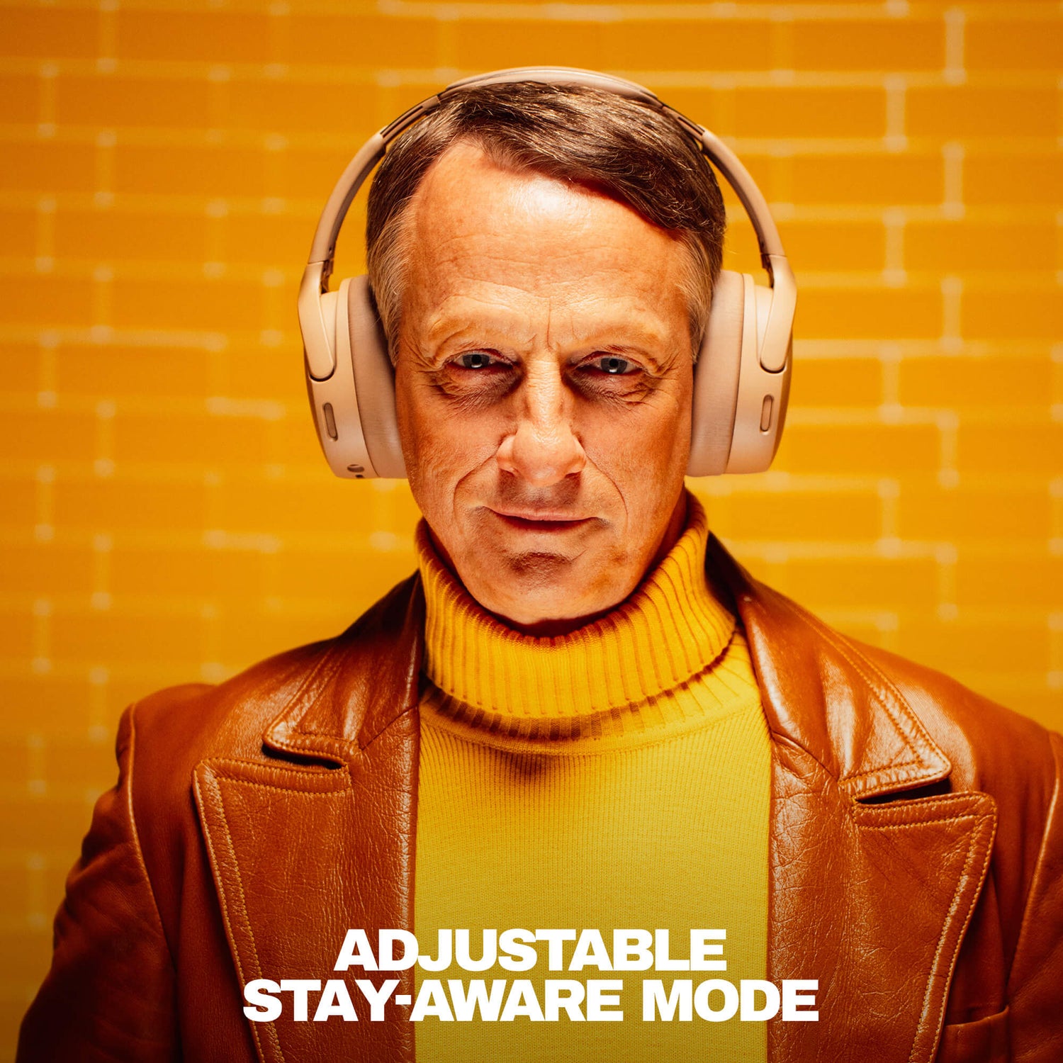 Tony Hawk wearing headphones with a text 'Adjustable Stay-Aware Mode' on an orange brick wall background | Primer