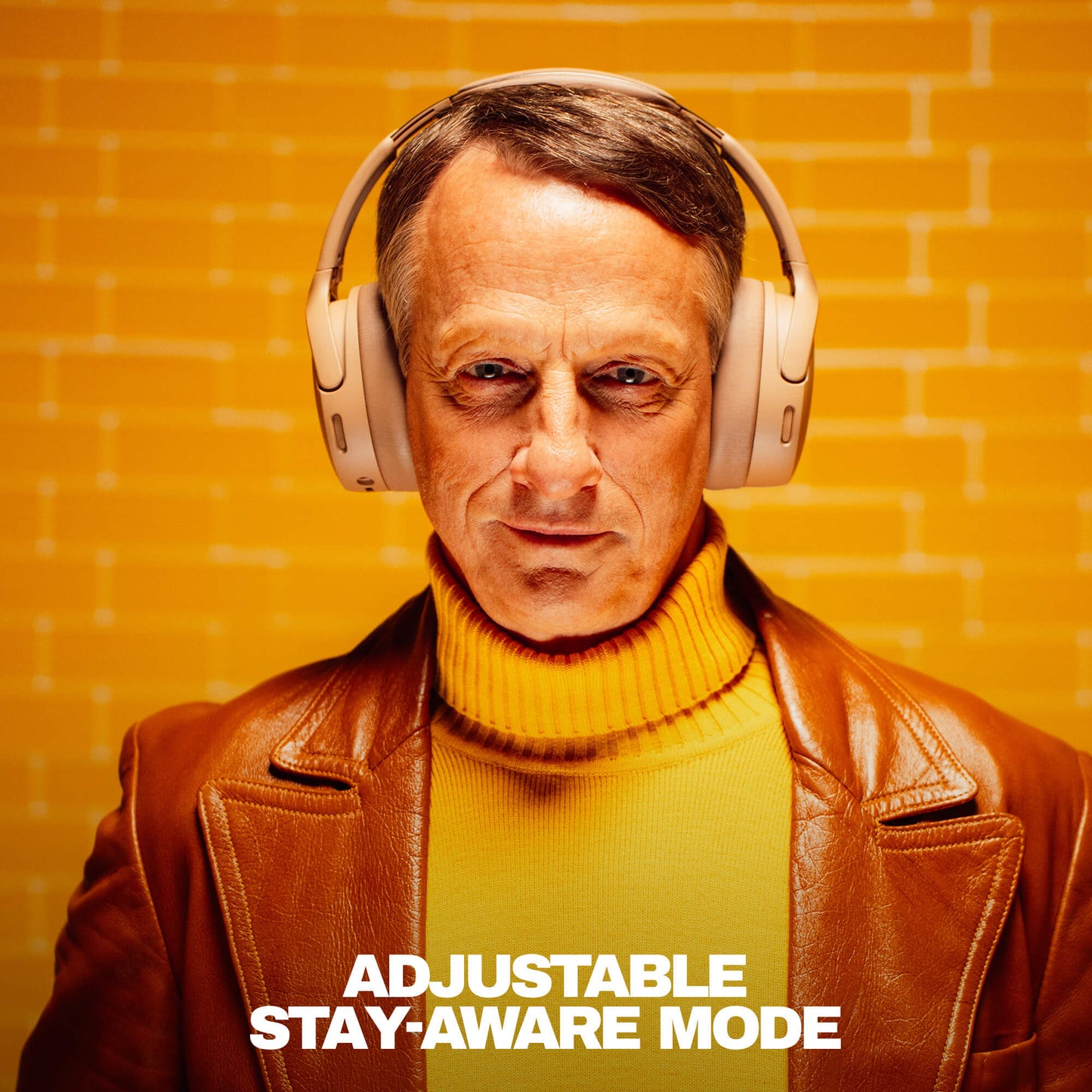 Tony Hawk wearing headphones with a text 'Adjustable Stay-Aware Mode' on an orange brick wall background | Primer