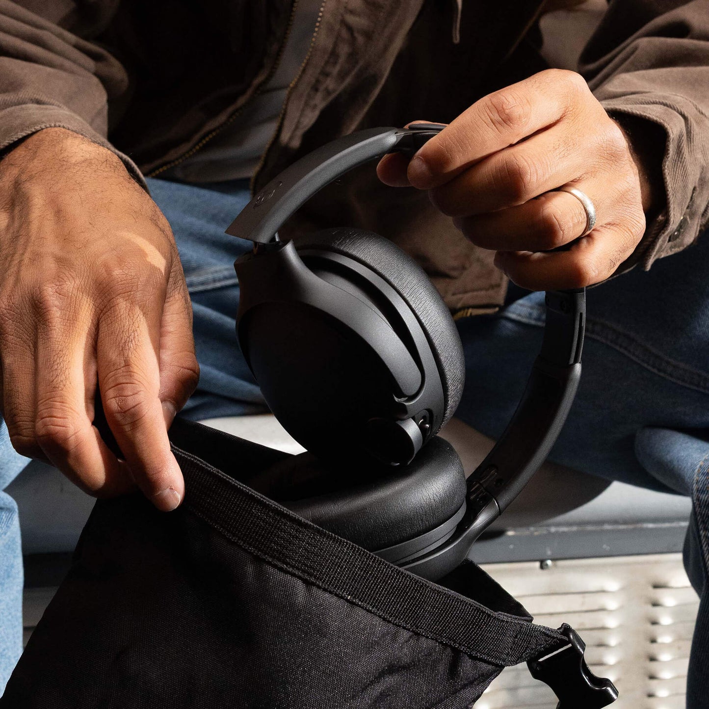 Person holding a pair of black headphones with a focus on the hands, travel case and product. | True Black