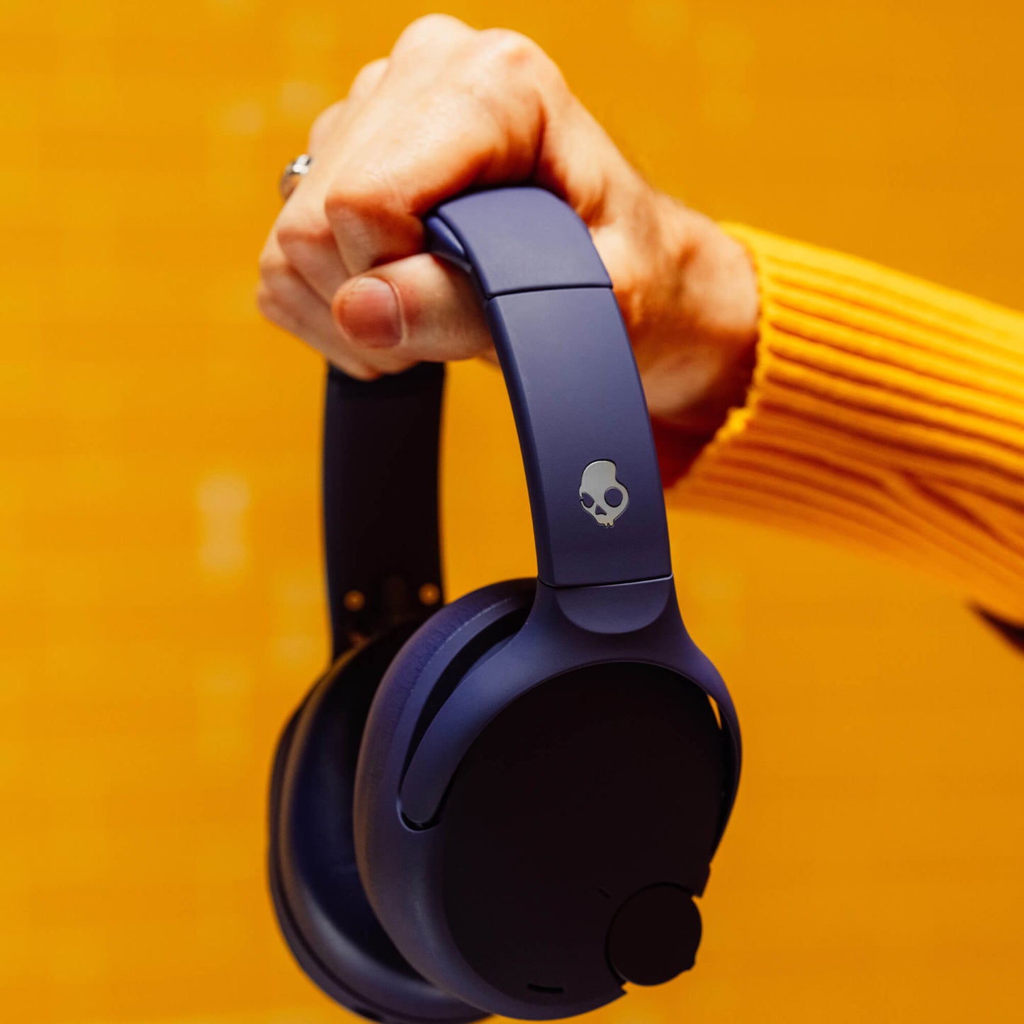 Person holding a pair of blue Crusher 720 headphones with a skull logo against an orange background | Future