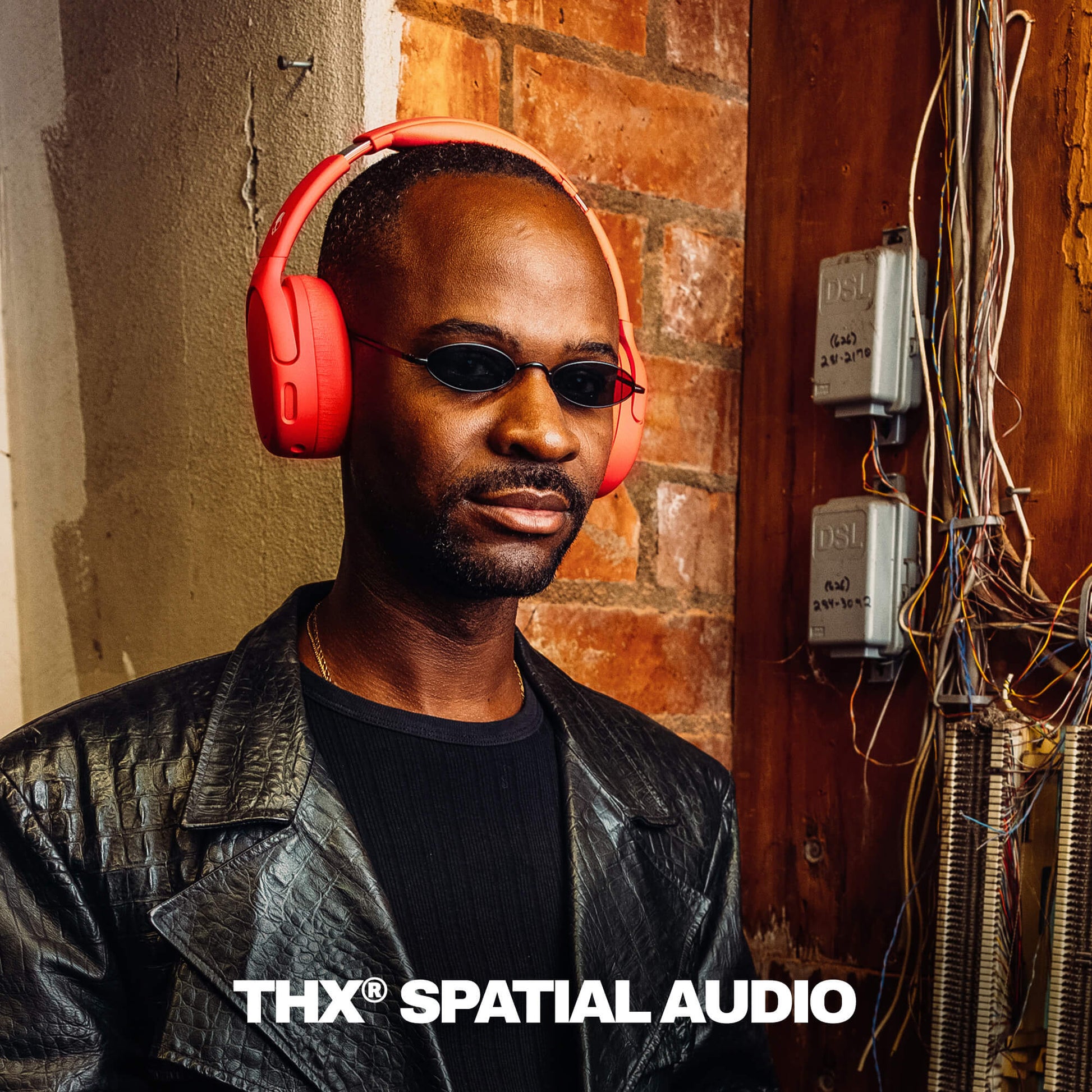 Man wearing red Crusher 720 headphones and sunglasses with 'THX Spatial Audio' branding against a brick wall. | Plasma