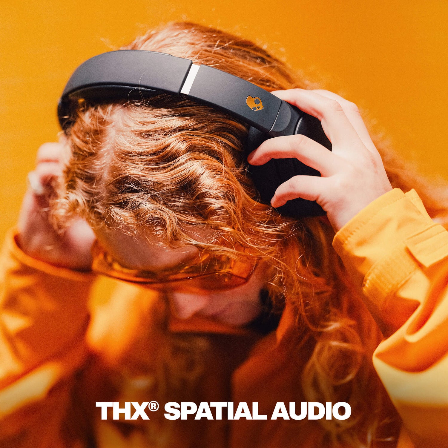 Person wearing black headphones with THX Spatial Audio branding against an orange background | True Black