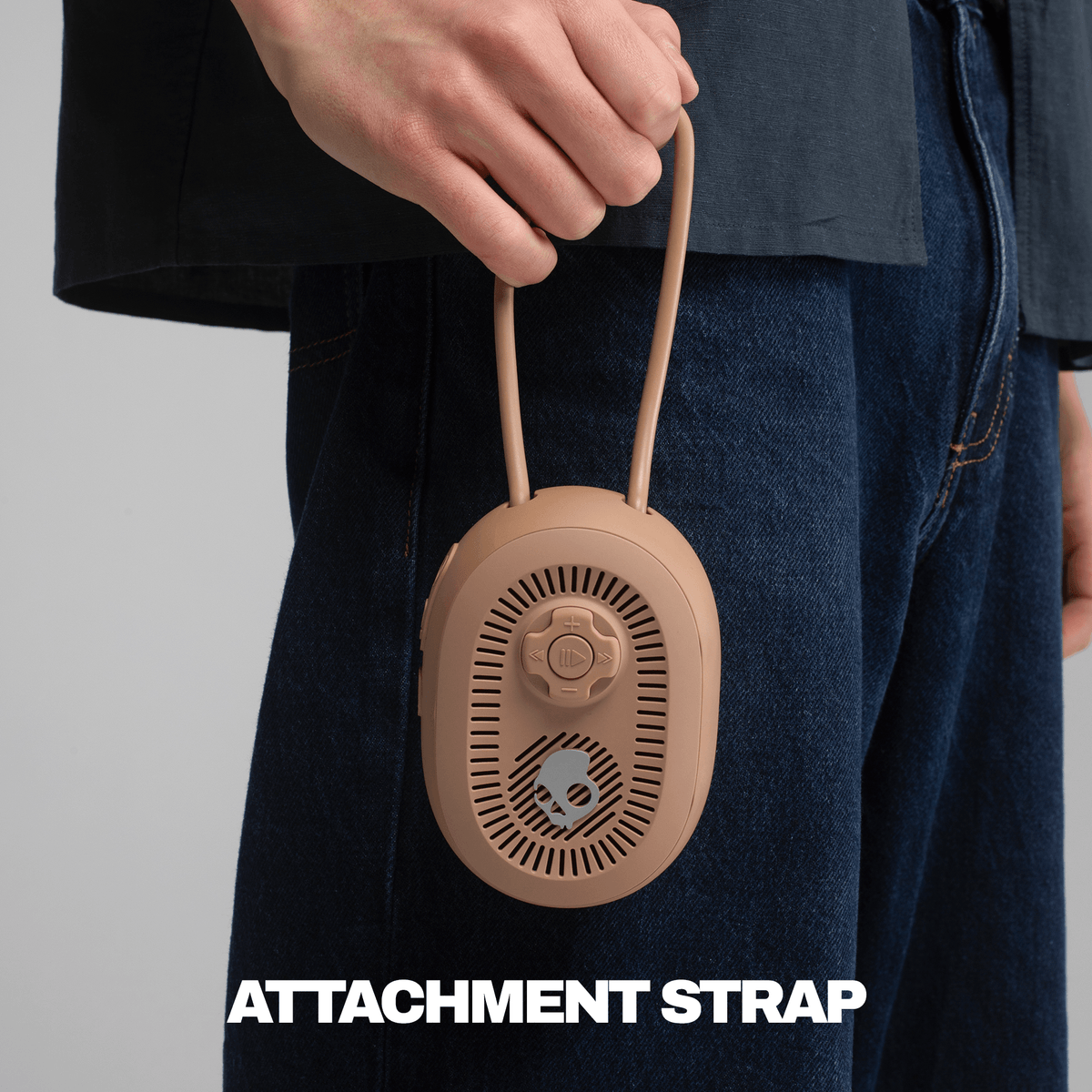 A person in a black shirt and blue jeans holds a tan session 540 speaker with an attached strap. | Primer