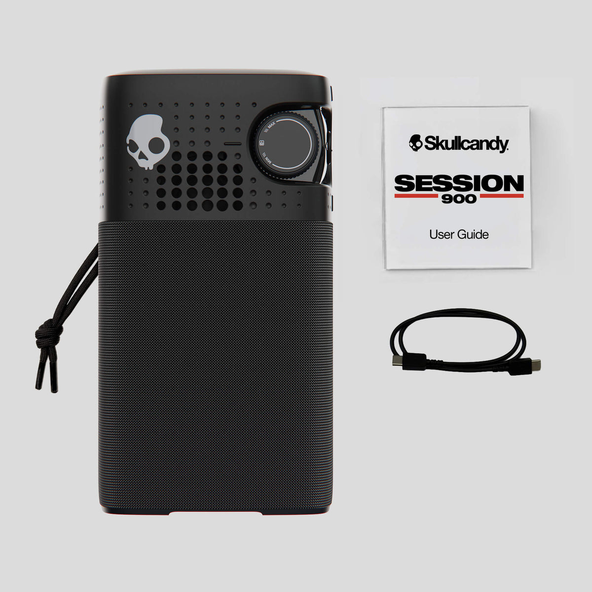 A black Skullcandy Session 900 portable speaker shown with its user guide booklet, charging cable, and carrying strap on a light gray background. | Cement