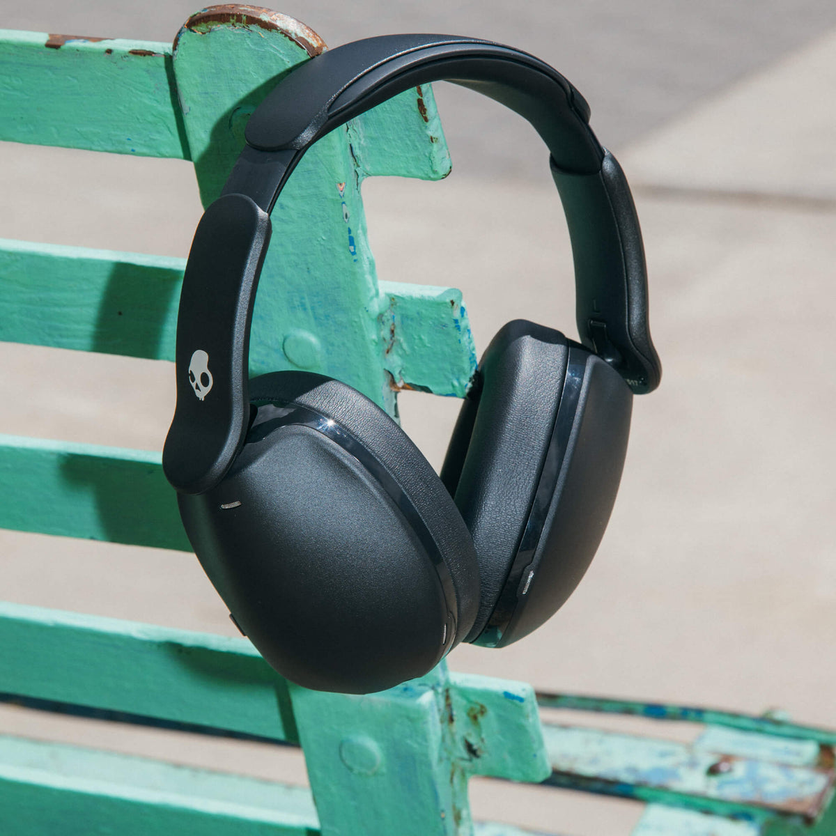 Black Hesh 360 over-ear headphones hanging on a green metal bench. | True Black