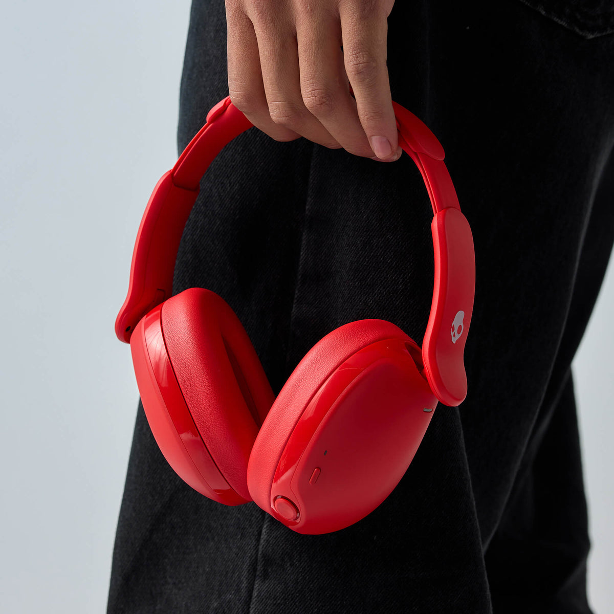 Red over-ear hesh 360 wireless headphones held by a person wearing black clothing, shown against a light gray background. | Plasma