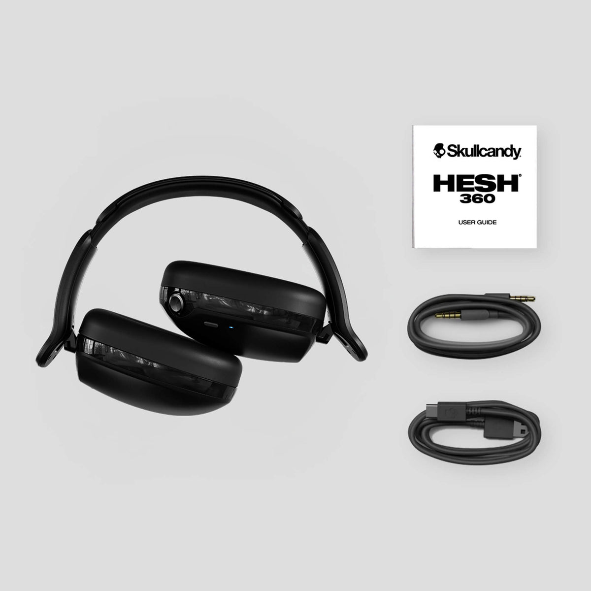 Black headphones with cables and Skullcandy HESH 360 user guide on a light gray background | Plasma