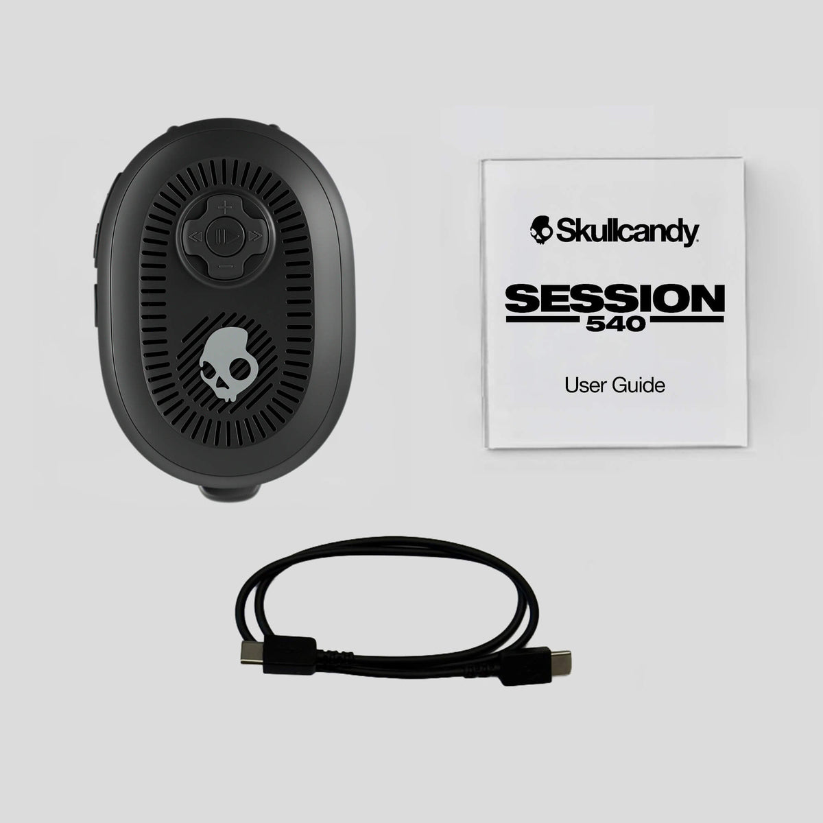 A black Skullcandy Session 540 wireless earbud charging case shown alongside its white user guide booklet and a black USB-C cable, all arranged on a light gray background. | Leopard