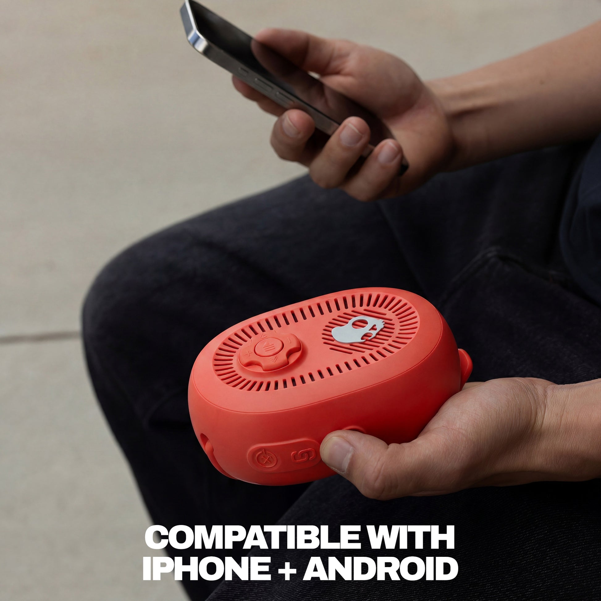 Person holding a red speaker and a smartphone with text 'Compatible with iPhone + Android' on a neutral background. | Plasma