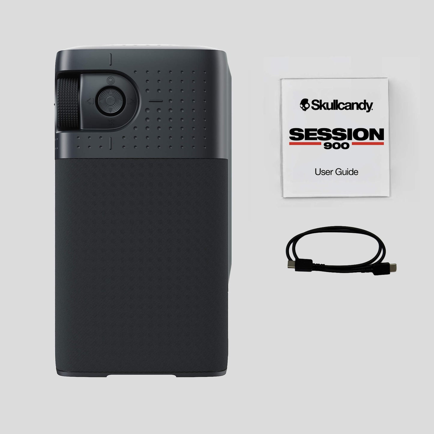A black Skullcandy Session 900 portable projector shown next to its user guide booklet and a black USB cable on a light gray background. | Primer