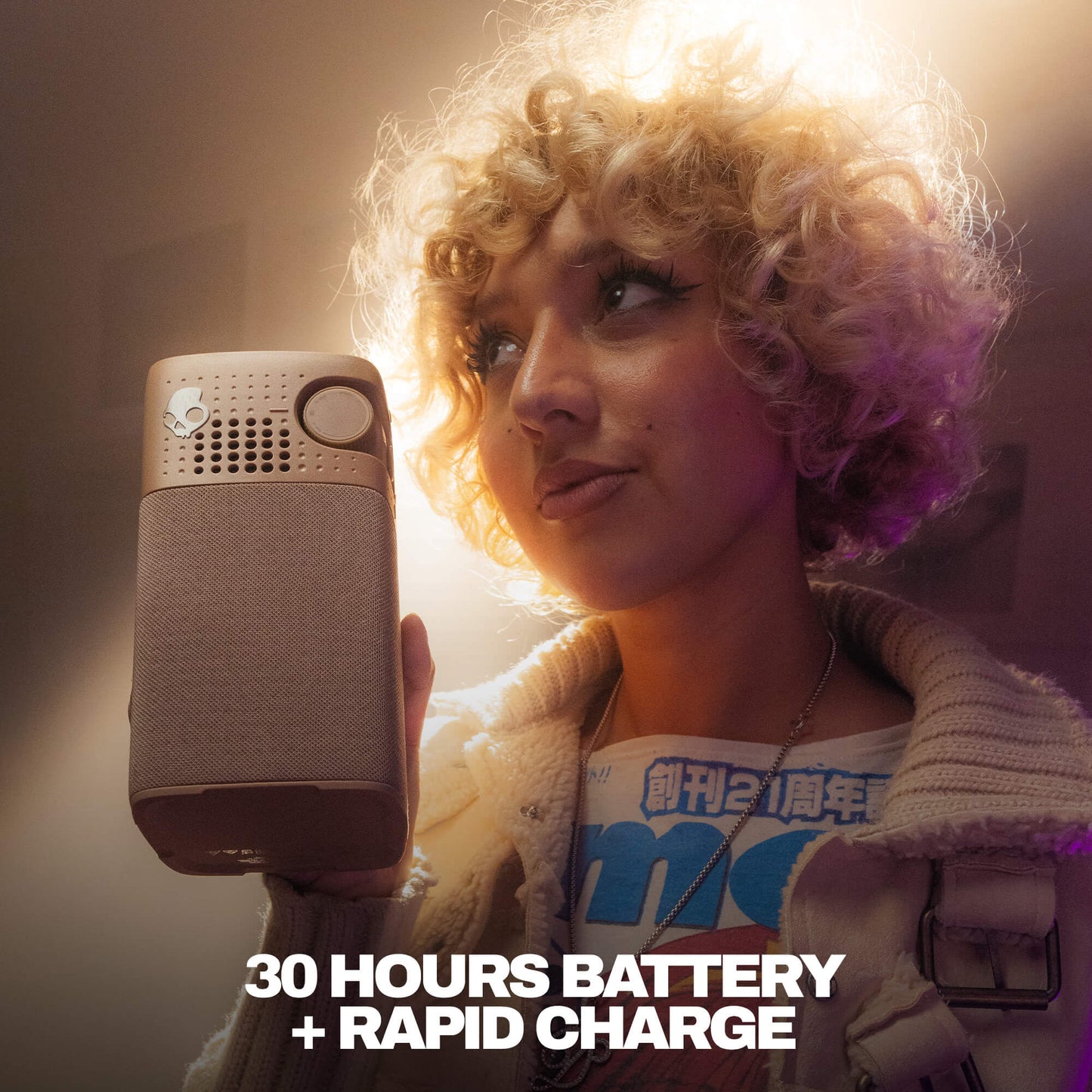 A woman with curly blonde hair holds a Session 900 speaker, with dramatic warm lighting and the text '30 HOURS BATTERY + RAPID CHARGE' at the bottom. | Primer