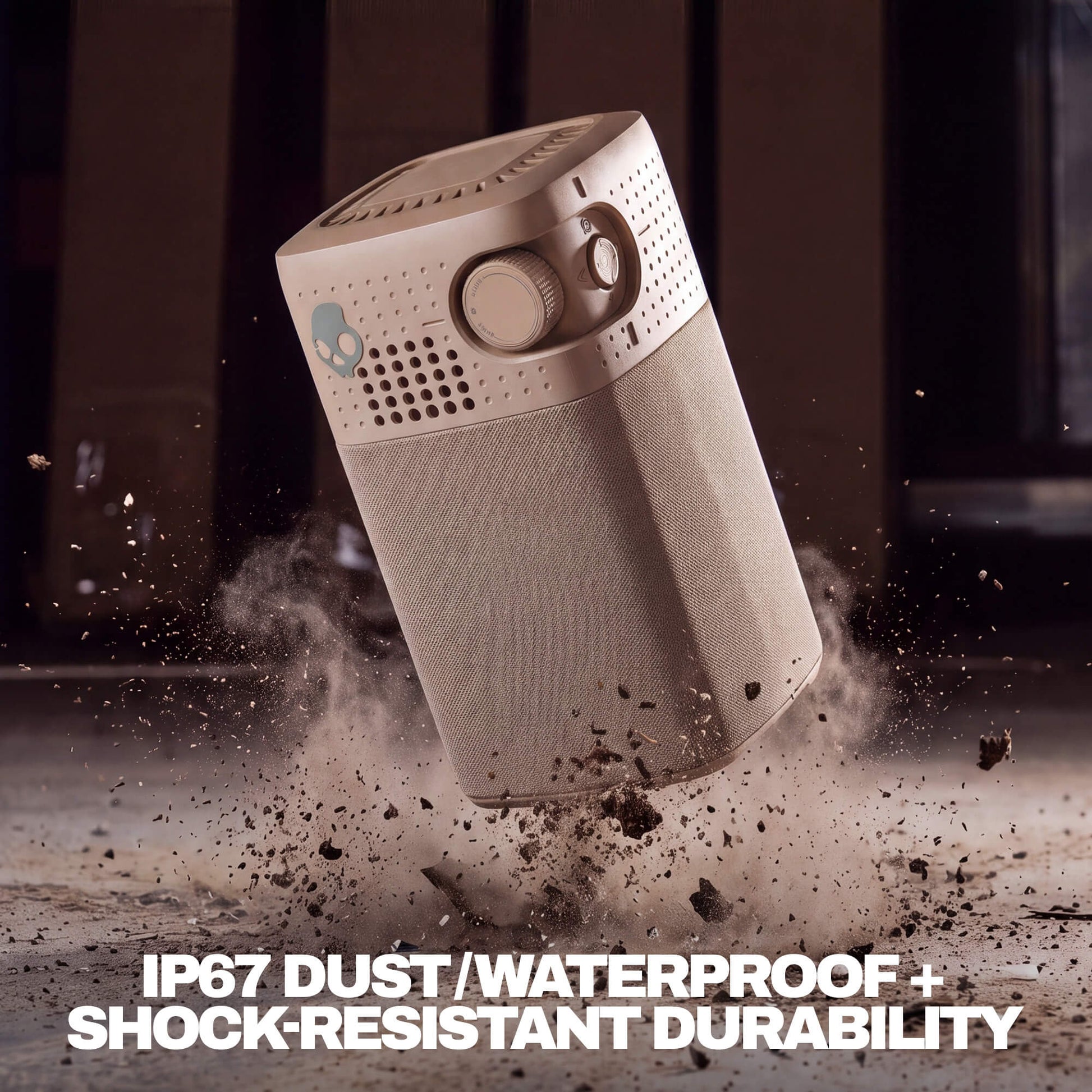 A Session 900 speaker with a textured lower body and perforated top grille, shown floating in midair with dramatic dust and debris around it. Bold white text at the bottom reads 'IP67 DUST/WATERPROOF + SHOCK-RESISTANT DURABILITY'. | Primer