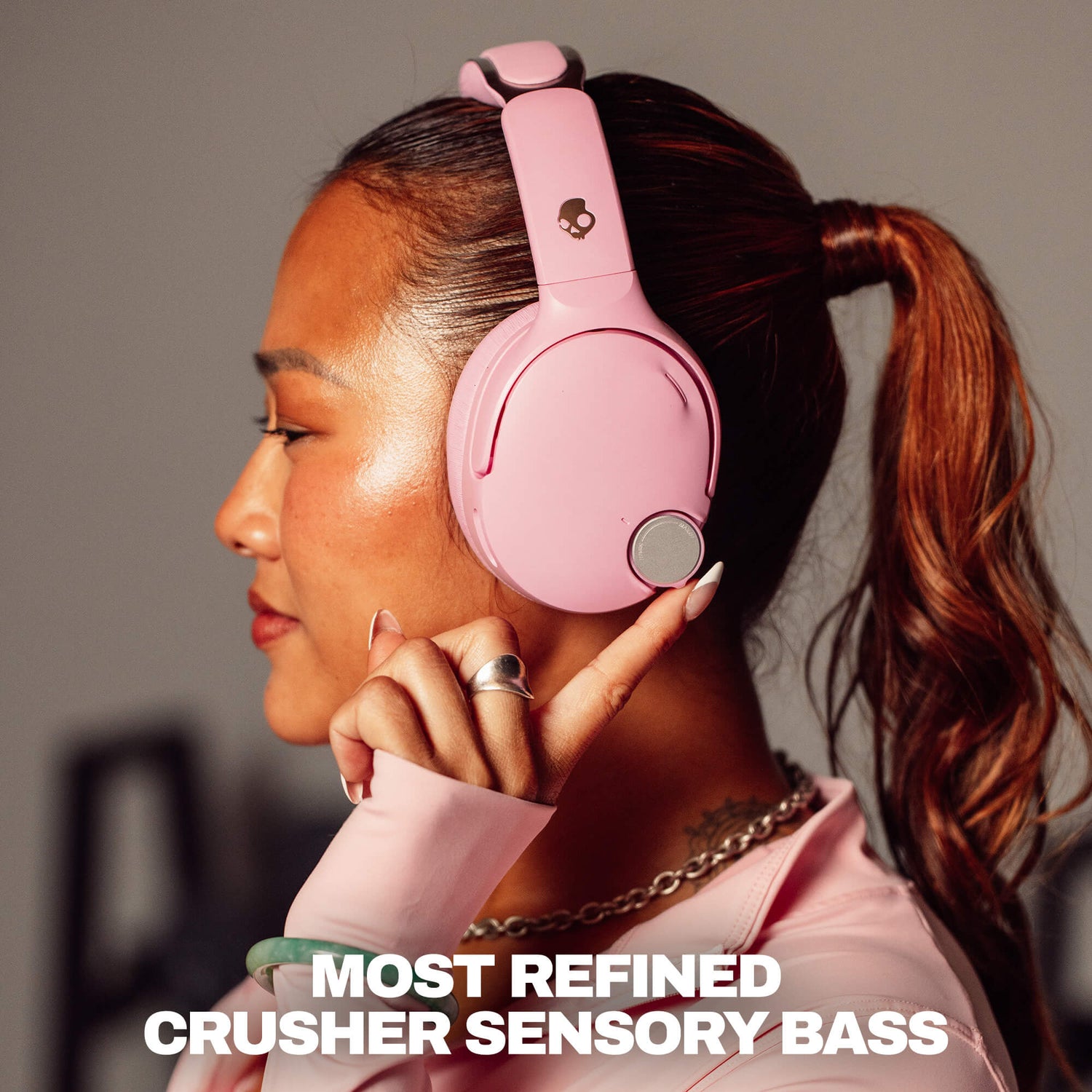 A woman in profile wearing light pink over-ear headphones with a small skull logo on the headband. The image includes text at the bottom reading 'MOST REFINED CRUSHER SENSORY BASS. | Candy