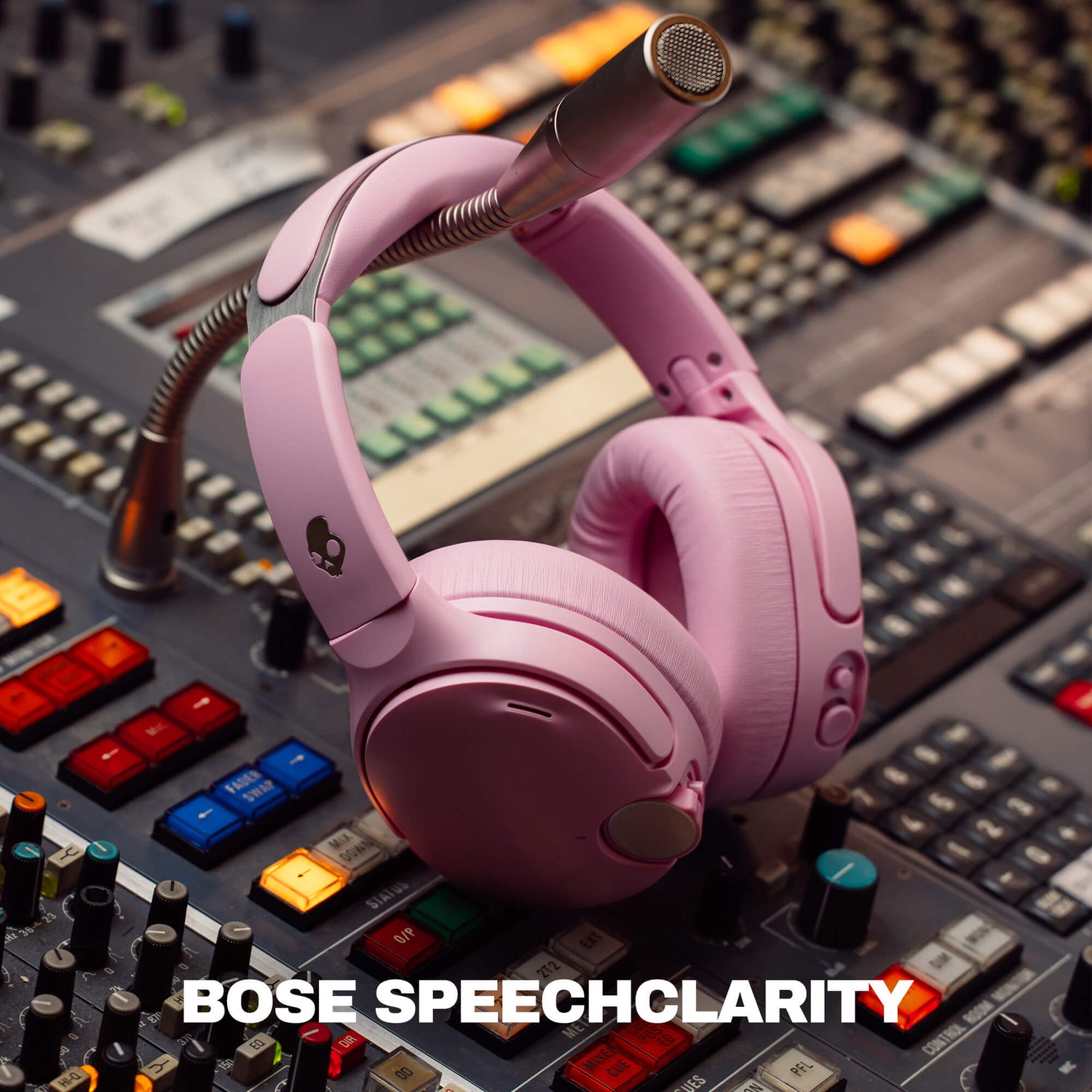 Pink over-ear headphones with a boom microphone resting on a professional audio mixing board. The text 'BOSE SPEECHCLARITY' is displayed at the bottom. | Candy