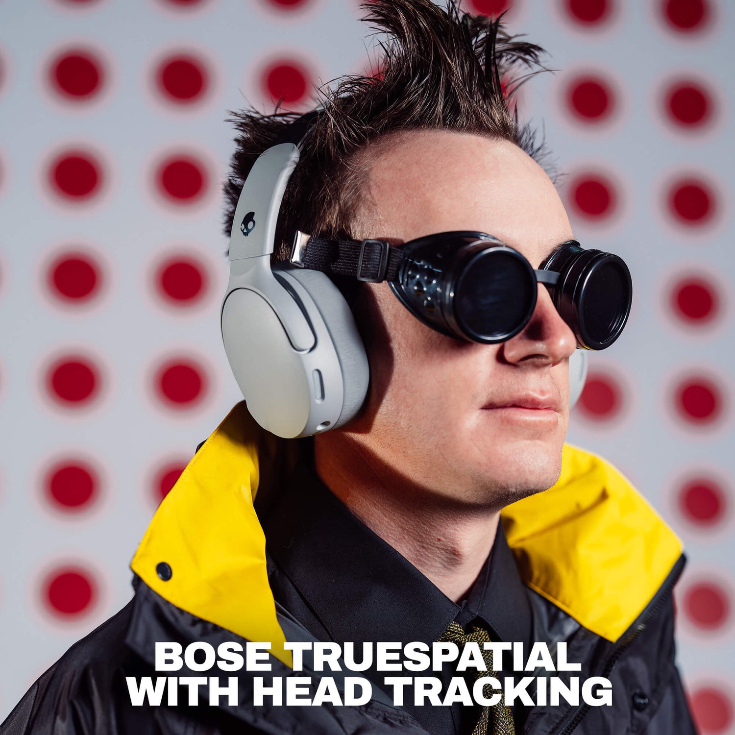 A man wearing white Bose TrueSpatial over-ear headphones with black straps and round black goggles, set against a white background with red polka dots. Text at the bottom reads 'BOSE TRUESPATIAL WITH HEAD TRACKING'. | Cement