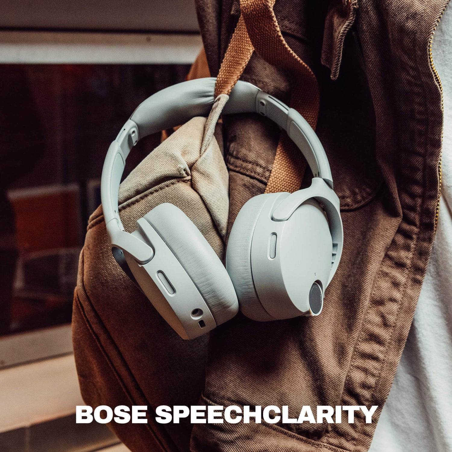Light gray Bose over-ear headphones hanging from a brown jacket, with the text 'BOSE SPEECHCLARITY' at the bottom. | Cement