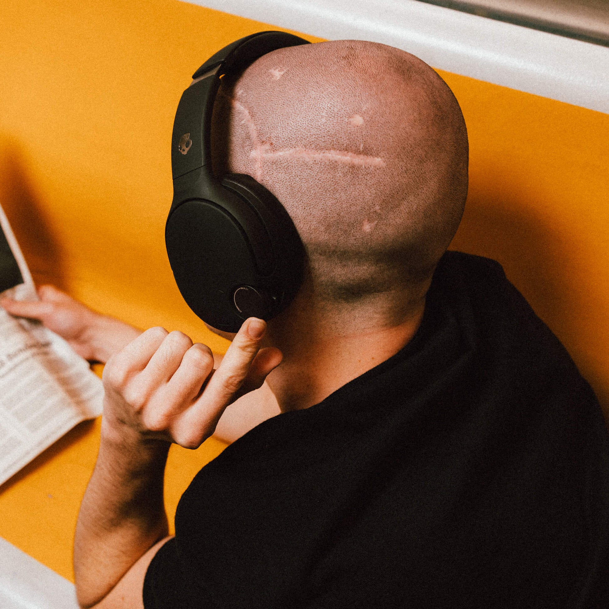 Person wearing black Crusher 720 headphones and reading a newspaper on an orange surface | True Black