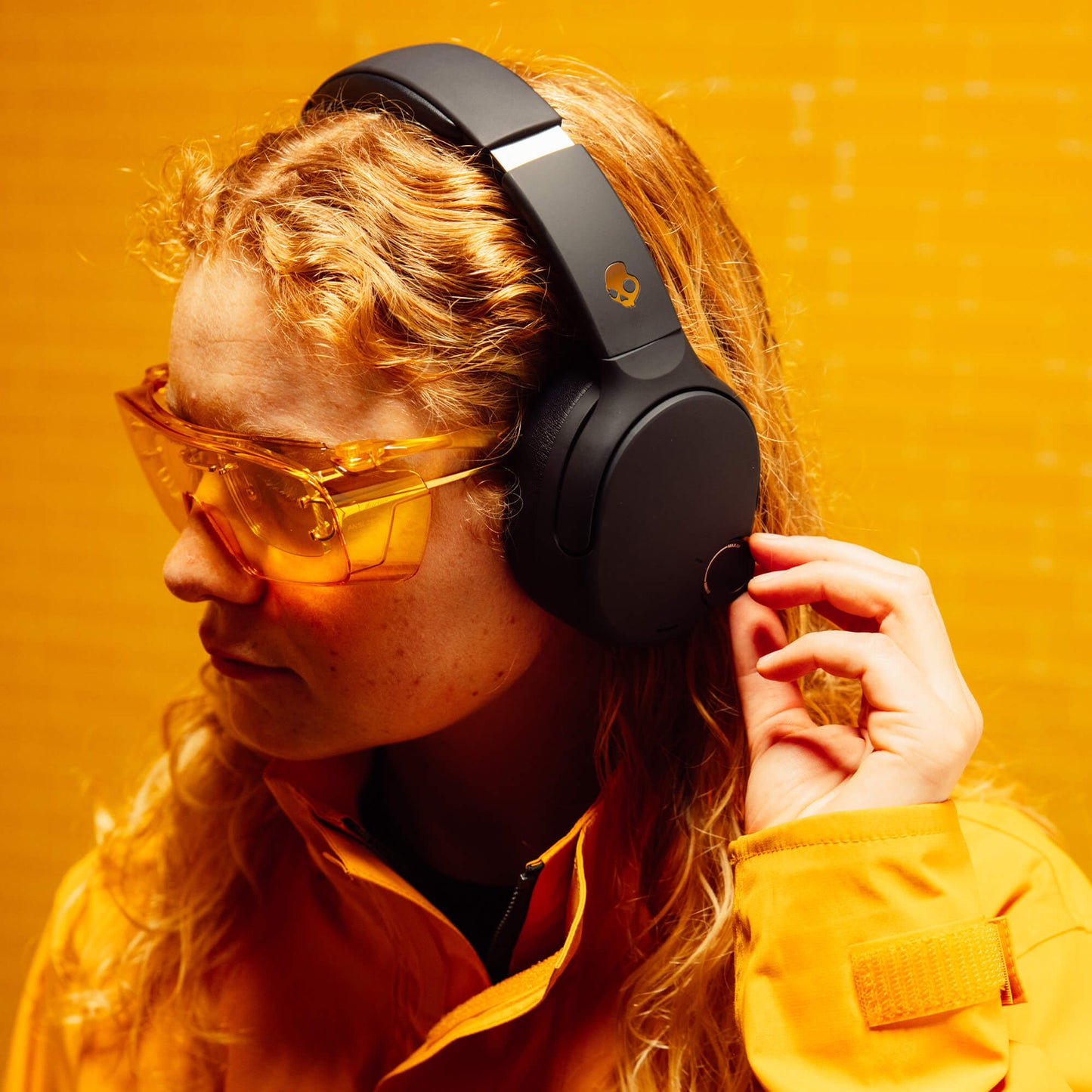 Person wearing black Crusher 720 headphones and yellow sunglasses against a yellow background | True Black