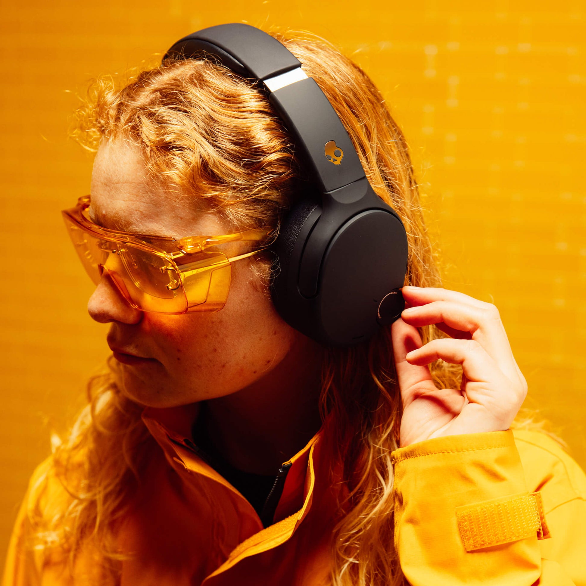 Person wearing black Crusher 720 headphones and yellow sunglasses against a yellow background | True Black