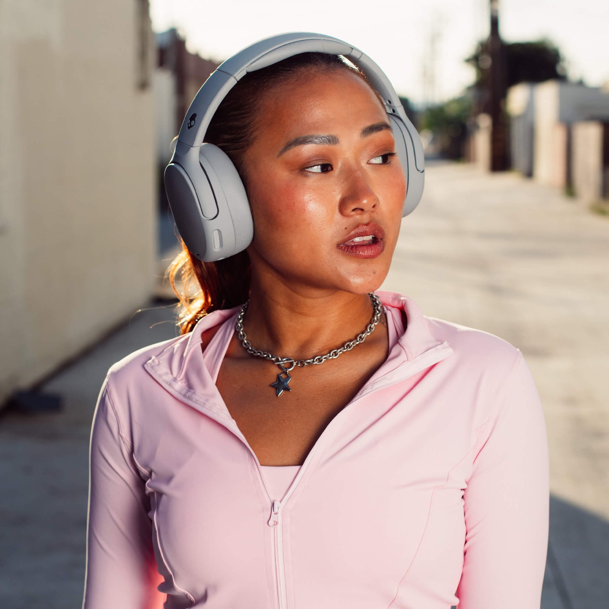 Woman wearing Crusher 720 headphones and a pink jacket on a street | Cement