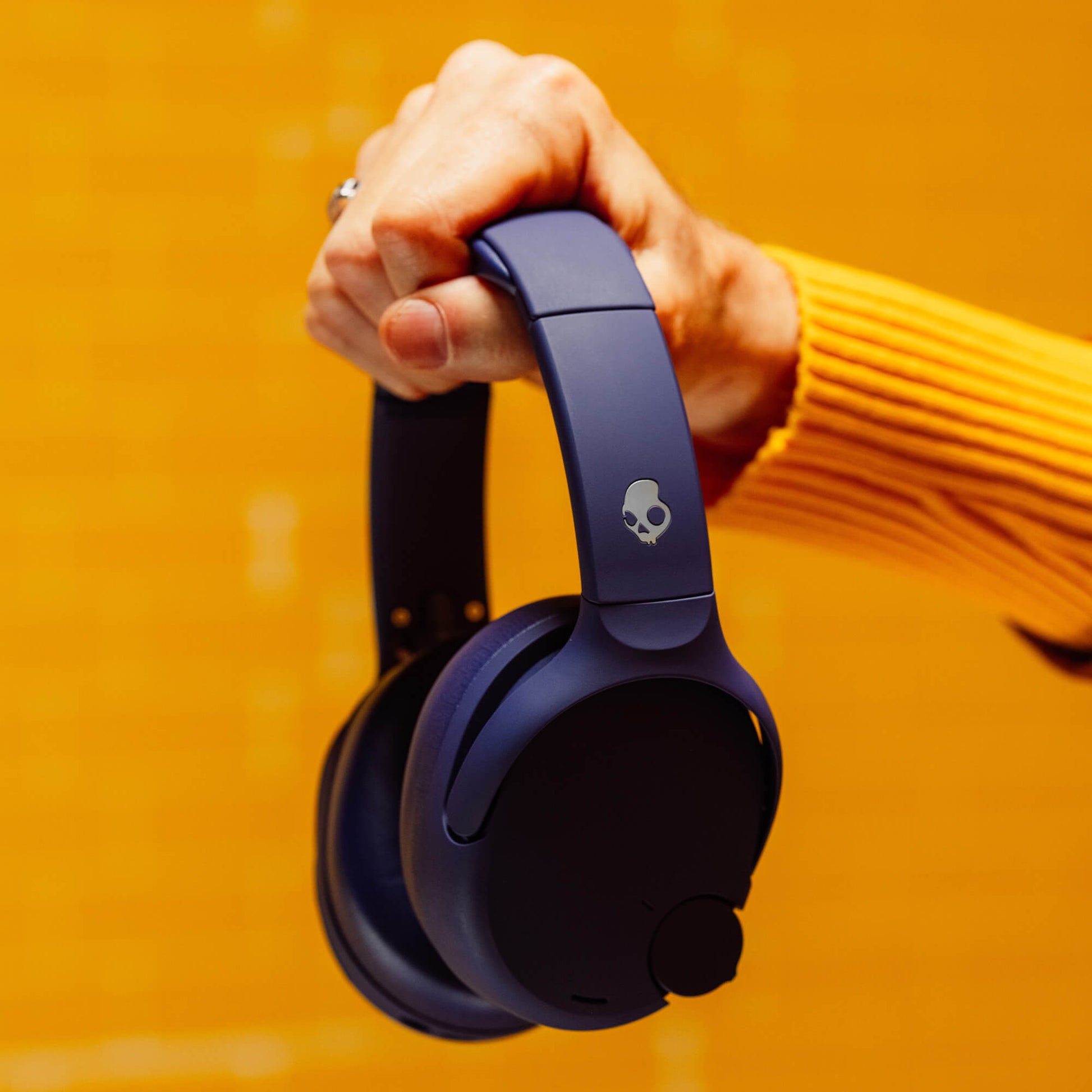 Person holding a pair of purple Crusher 720 headphones with a skull logo against an orange background | Future